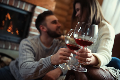 Photo of Couple with glasses of wine near fireplace indoors, focus on hands. Winter vacation