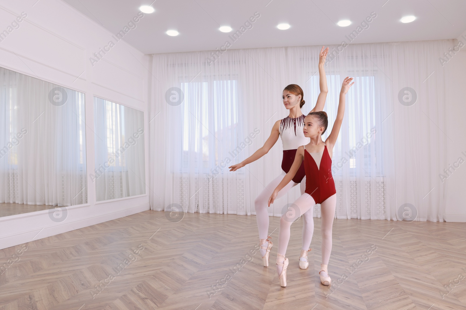 Photo of Little ballerina and her teacher practicing dance moves in studio. Space for text 