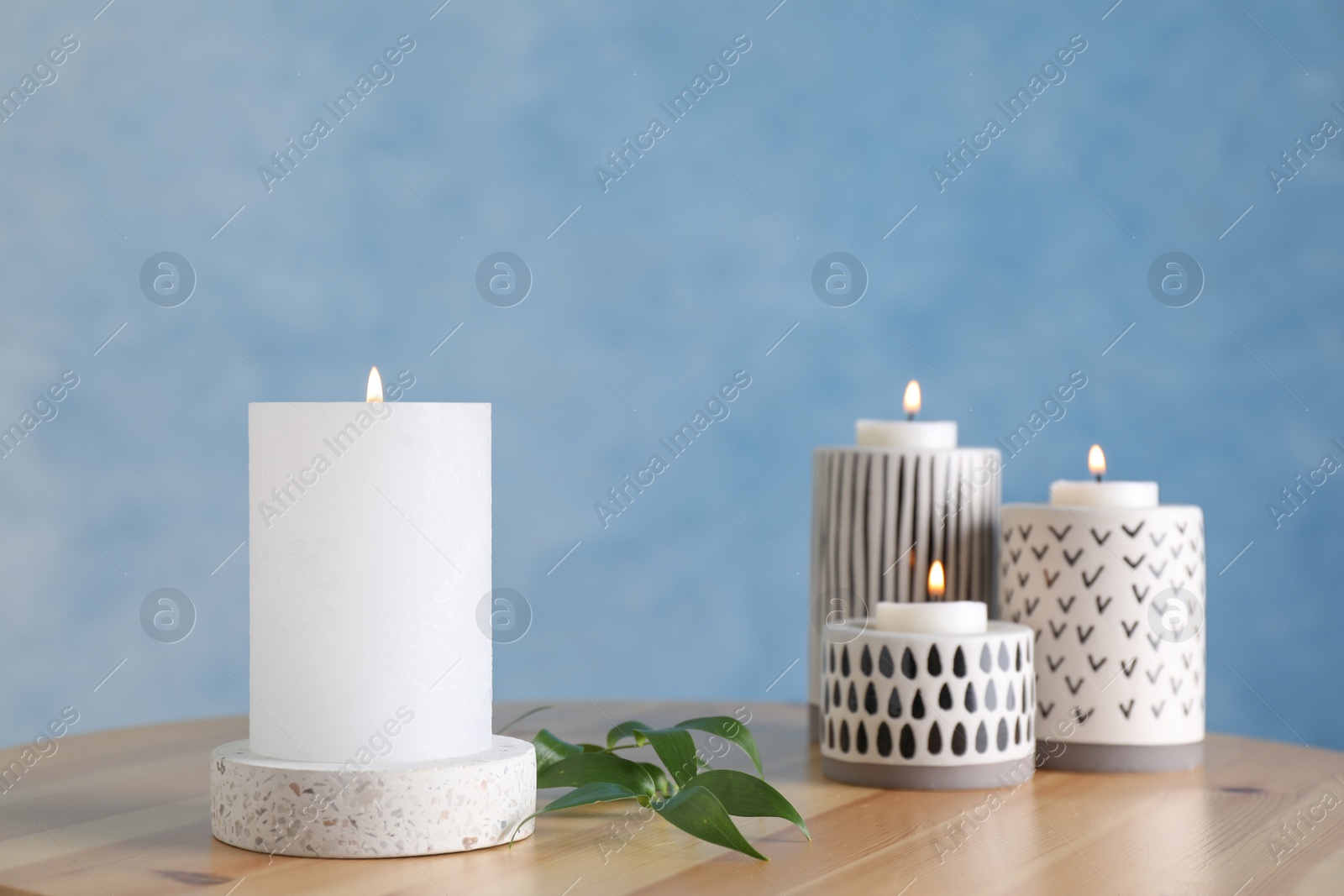 Photo of Burning candles on wooden table against light blue background