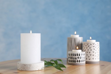 Photo of Burning candles on wooden table against light blue background
