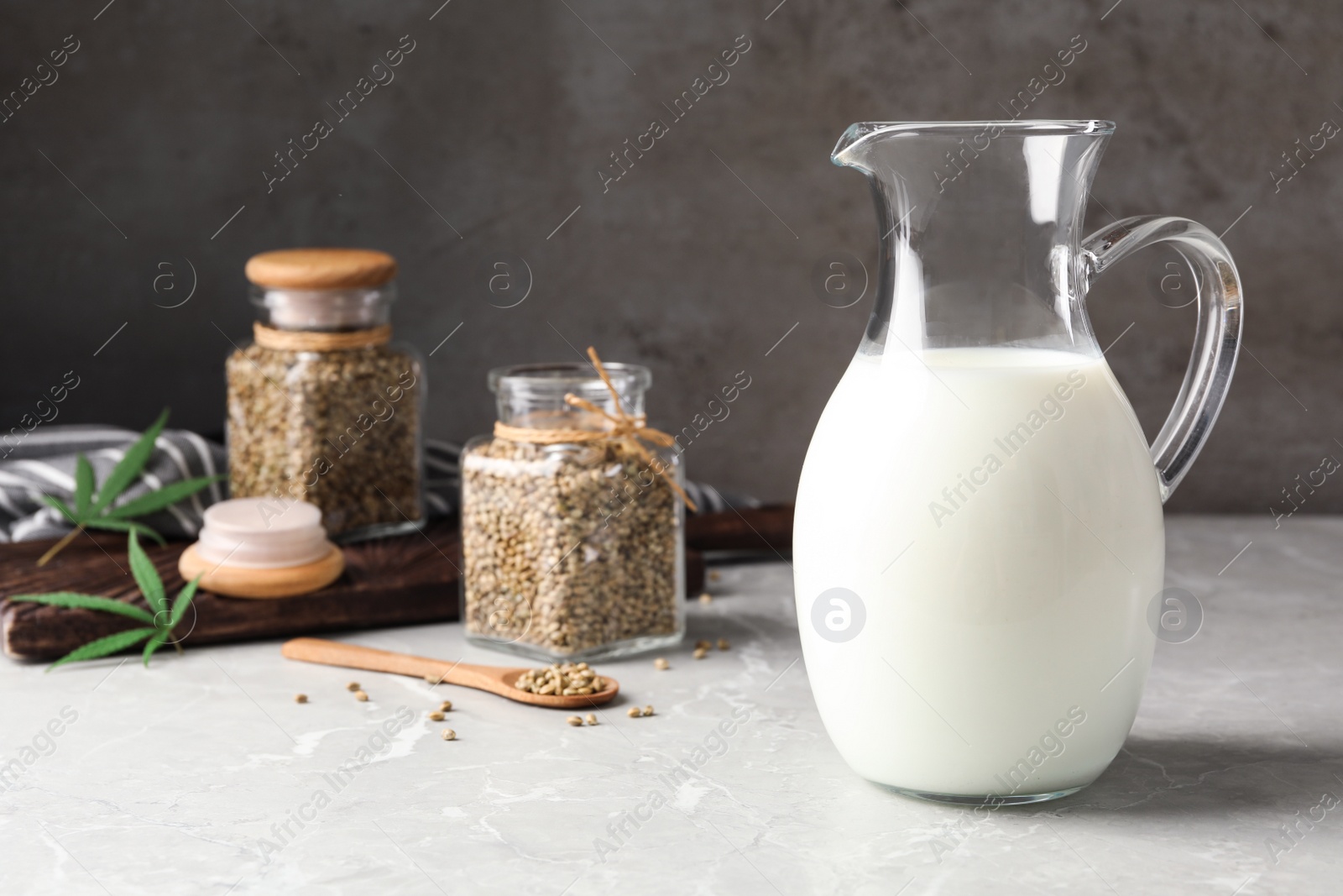 Photo of Composition with pitcher of hemp milk on marble table against grey background. Space for text