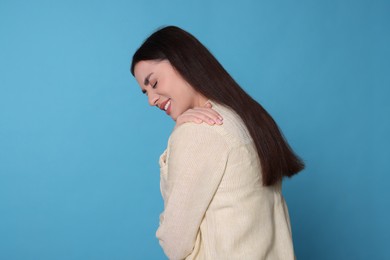 Photo of Young woman suffering from pain in shoulder on light blue background, space for text. Arthritis symptoms