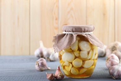 Photo of Garlic with honey in glass jar and unpeeled cloves on grey wooden table. Space for text