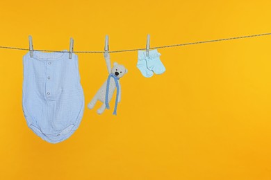 Photo of Baby clothes and toy drying on laundry line against orange background, space for text