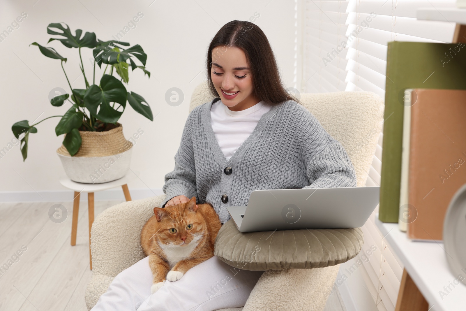 Photo of Happy woman working with laptop and petting cute cat at home