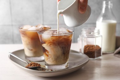 Photo of Woman pouring milk into glass with refreshing iced coffee at light table, closeup