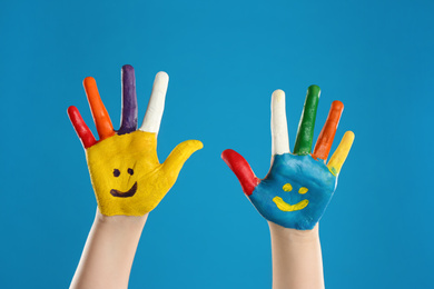 Photo of Kid with smiling faces drawn on palms against blue background, closeup