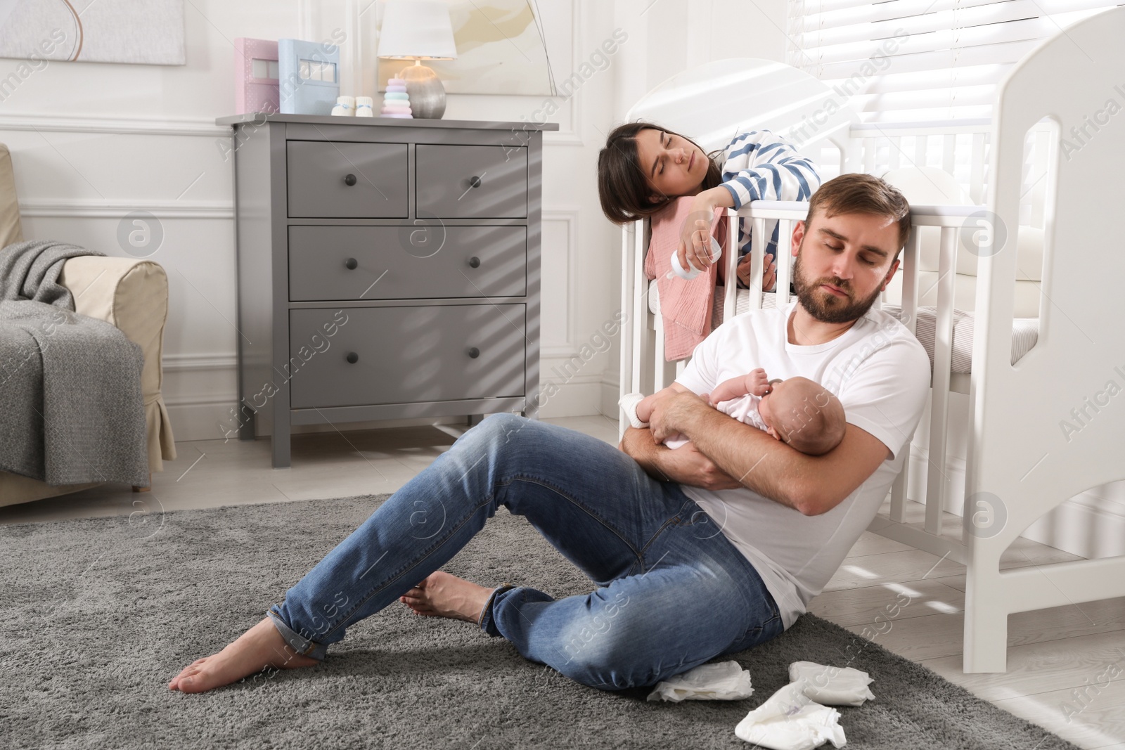 Photo of Tired young parents with their baby sleeping in children's room