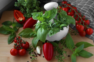 Photo of Mortar with fresh herbs, cherry tomatoes and pepper on wooden table