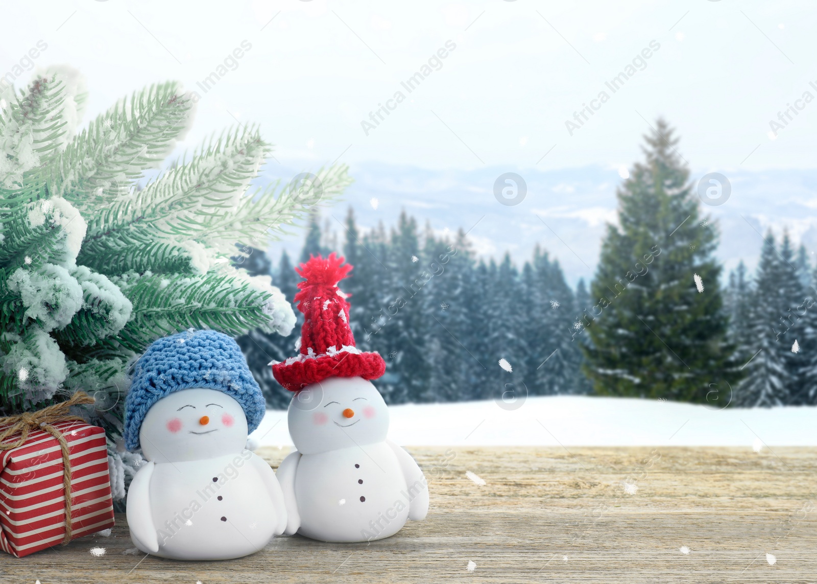 Image of Cute decorative snowmen, gift box and fir tree on wooden table outdoors, space for text