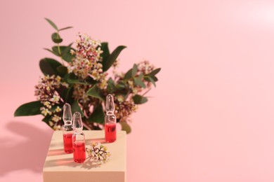 Photo of Stylish presentation of skincare ampoules and flowers on pink background, closeup. Space for text