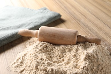 Photo of Pile of flour and rolling pin on wooden table, closeup