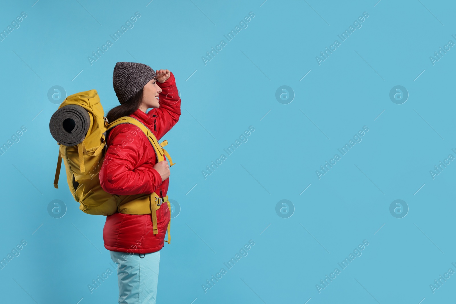 Photo of Smiling young woman with backpack on light blue background, space for text. Active tourism