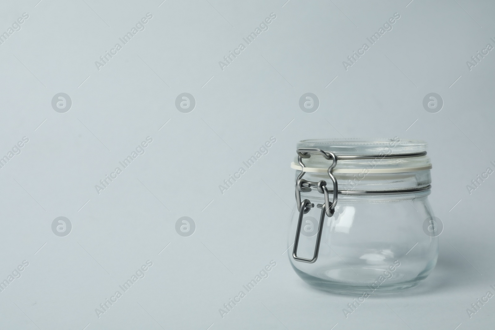 Photo of Closed empty glass jar on light background, space for text