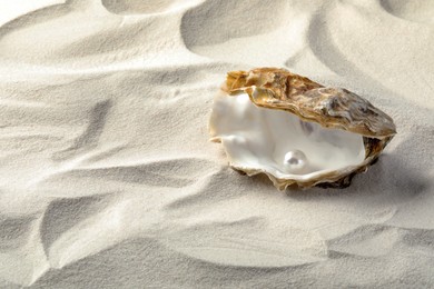 Photo of Open oyster with white pearl on sand, space for text