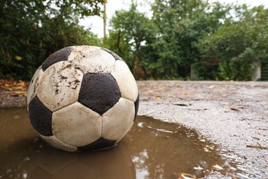 Dirty soccer ball in muddy puddle, space for text