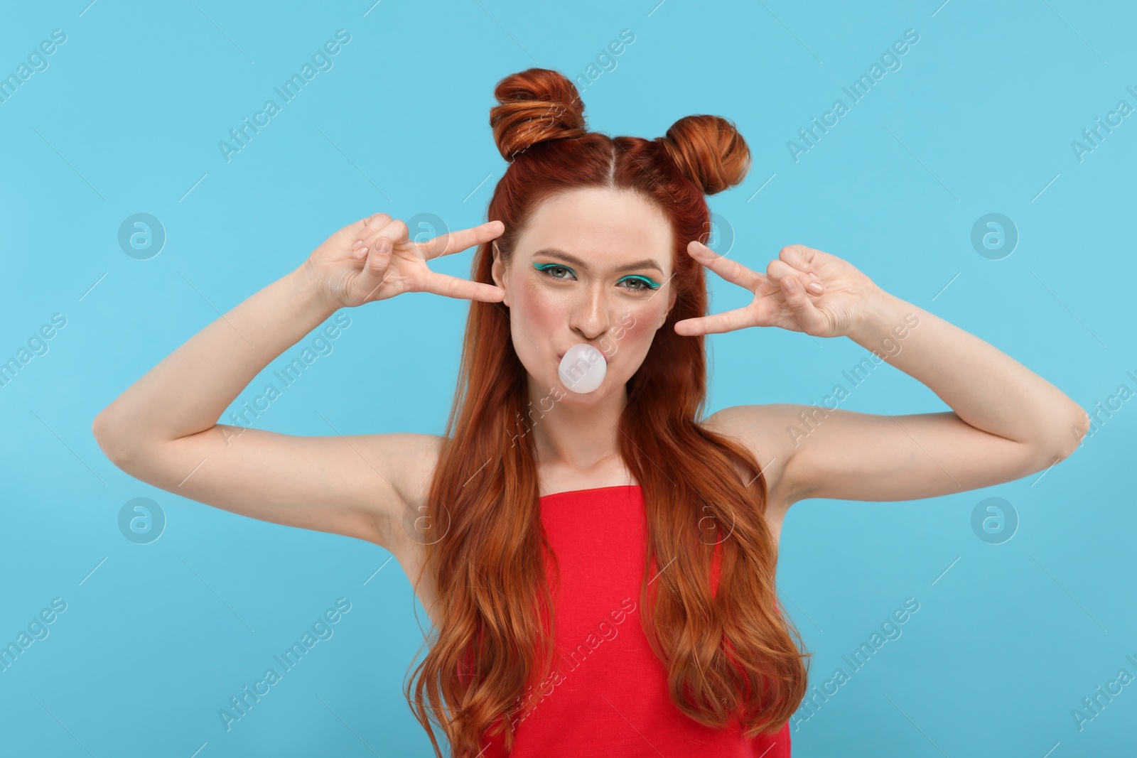 Photo of Portrait of beautiful woman with bright makeup blowing bubble gum and gesturing on light blue background