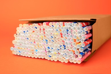 Box with many paper drinking straws on orange background