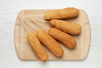 Photo of Delicious deep fried corn dogs on white wooden table, top view