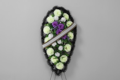 Photo of Funeral wreath of plastic flowers with ribbon on grey background