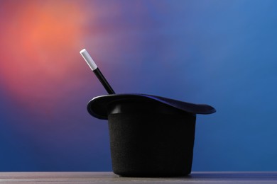 Photo of Magician's hat and wand on wooden table against color background