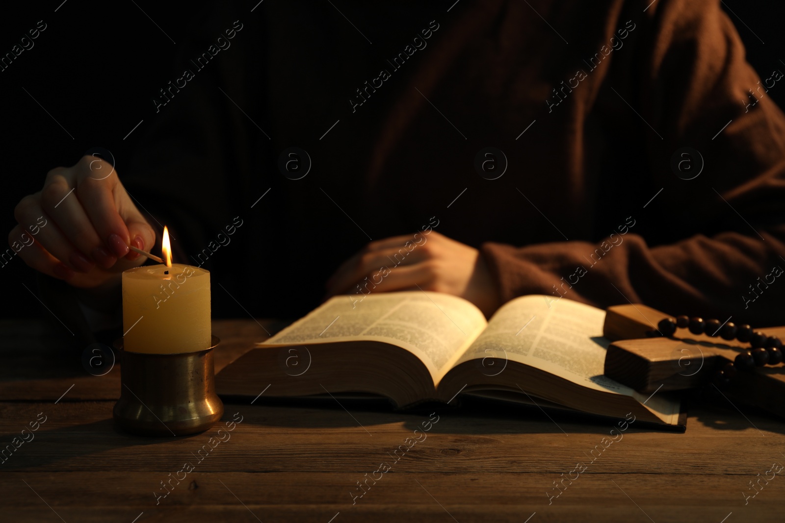 Photo of Woman praying at table with burning candle and Bible, closeup