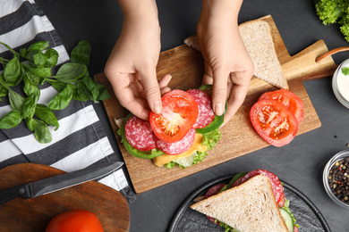 Photo of Woman adding tomato to sandwich at black table, top view