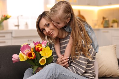 Little daughter congratulating her mom with Mother`s Day at home. Woman holding bouquet of beautiful tulips