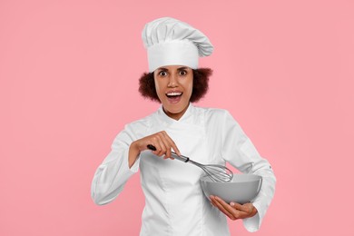Photo of Emotional female chef in uniform with whisk and bowl on pink background
