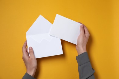 Woman with letter envelope and card at orange table, top view. Space for text