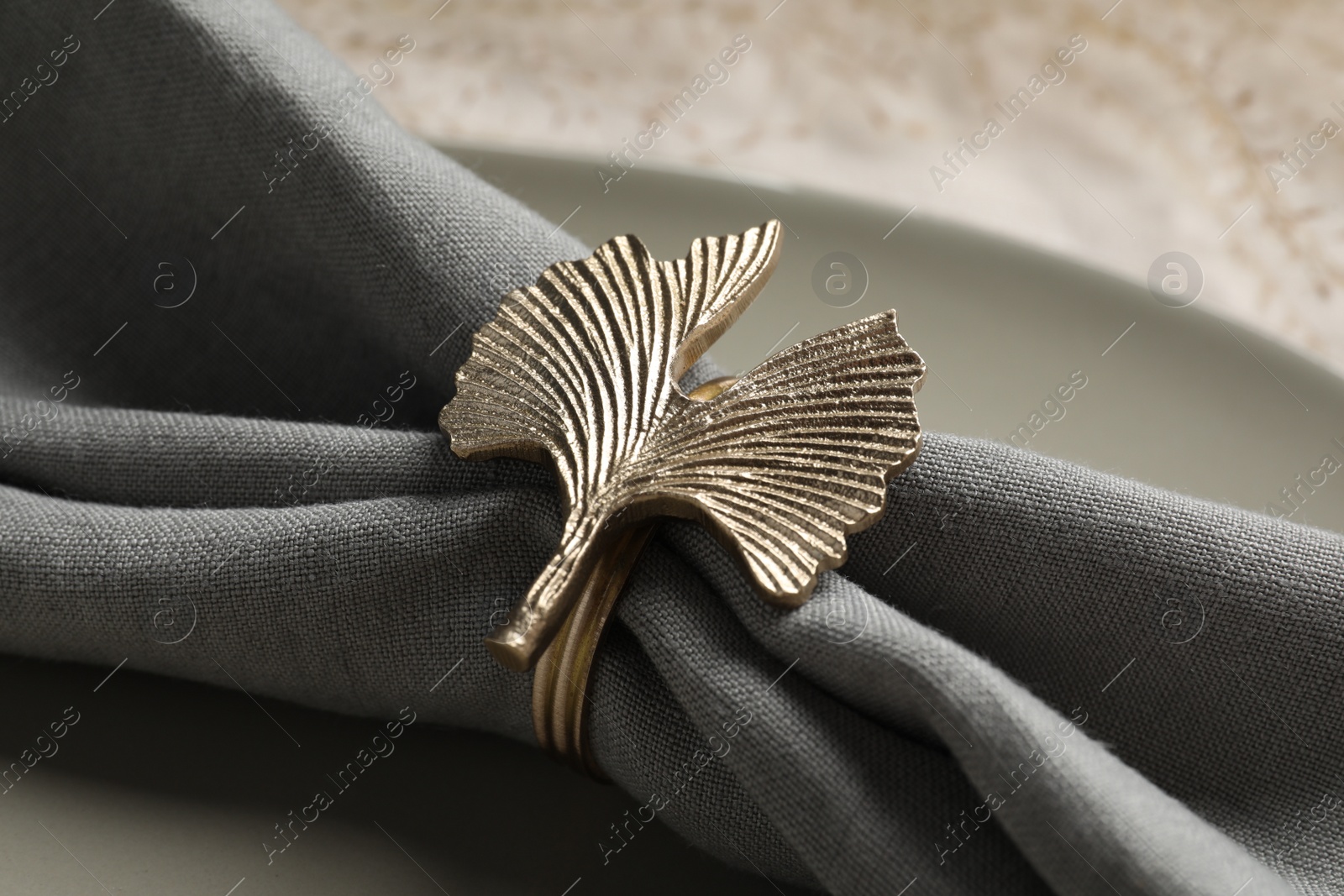 Photo of Gray fabric napkin and decorative ring for table setting on plate, closeup