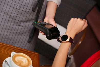 Photo of Woman making payment with smart watch in cafe, closeup