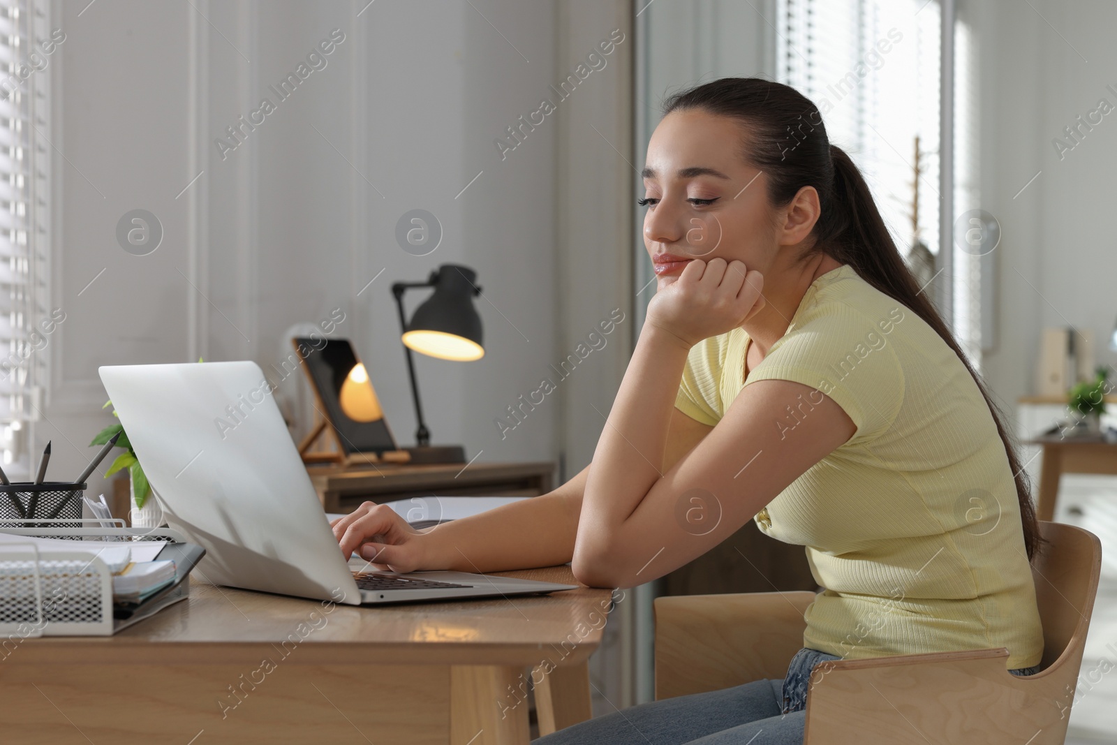 Photo of Young woman with poor posture using laptop at table indoors