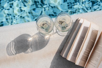 Glasses of tasty wine and open book on swimming pool edge, above view