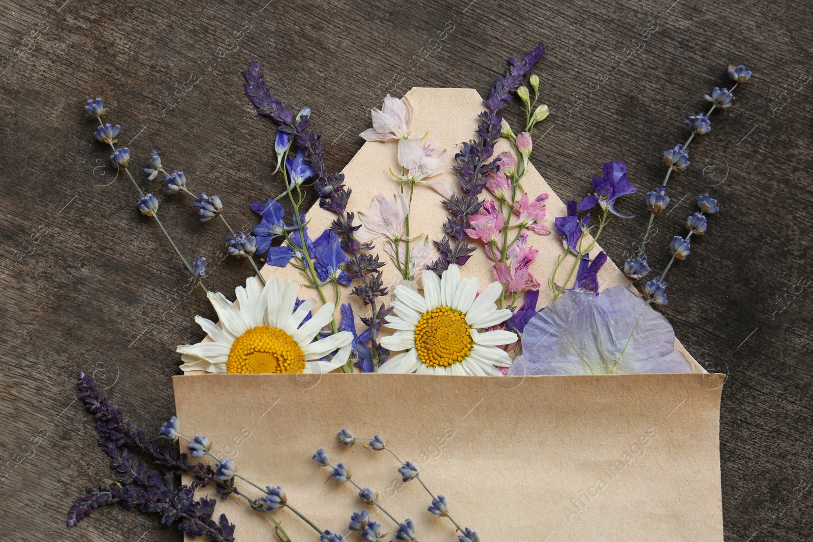 Photo of Flat lay composition with beautiful dried flowers in envelope on wooden background