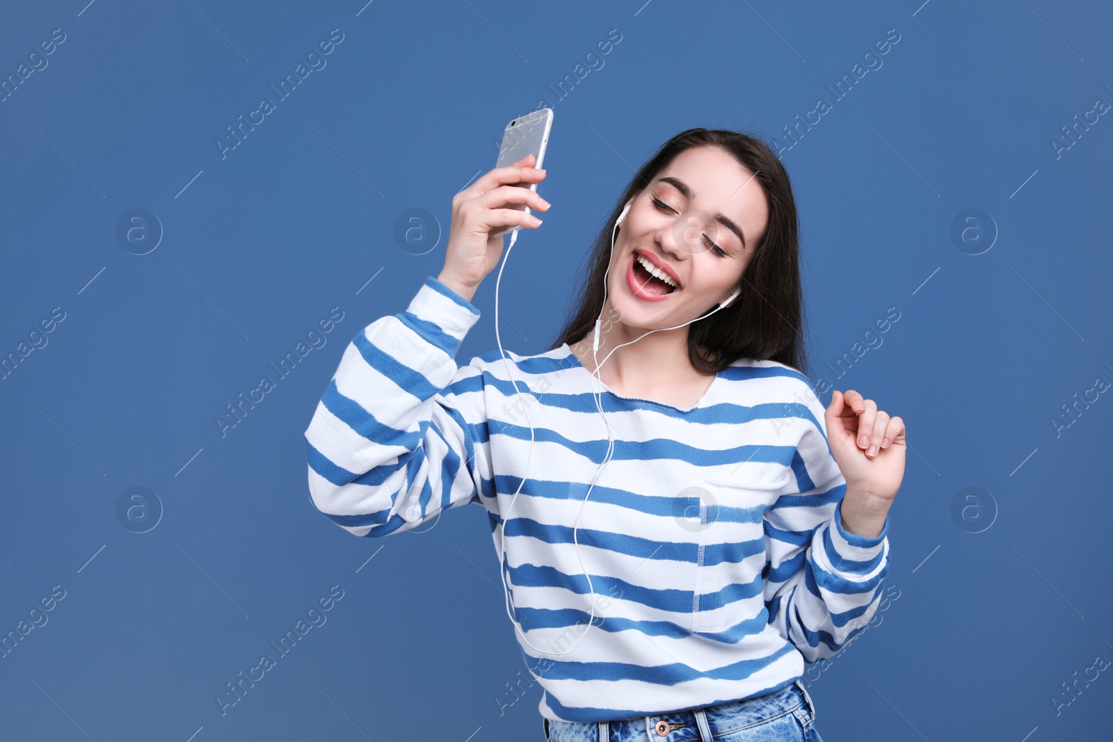 Photo of Young woman using phone for listening to music on color background