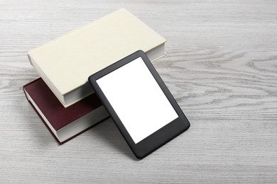 Photo of Portable e-book reader and hardcover books on white wooden table