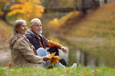 Photo of Affectionate senior couple with dry leaves in autumn park, space for text