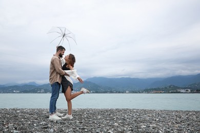 Photo of Young couple with umbrella enjoying time together under rain on beach, space for text