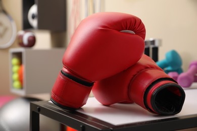 Photo of Red boxing gloves on white table in room with other sports equipment