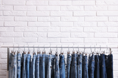 Photo of Rack with stylish jeans near brick wall. Space for text