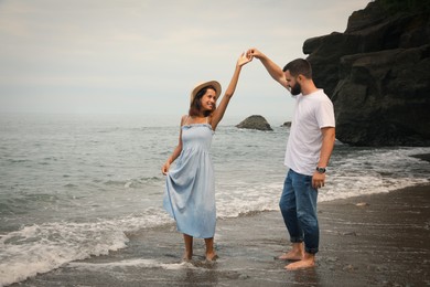 Photo of Happy young couple dancing on beach near sea. Space for text