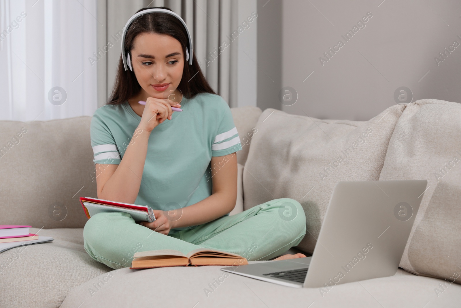 Photo of Young woman watching webinar on sofa at home