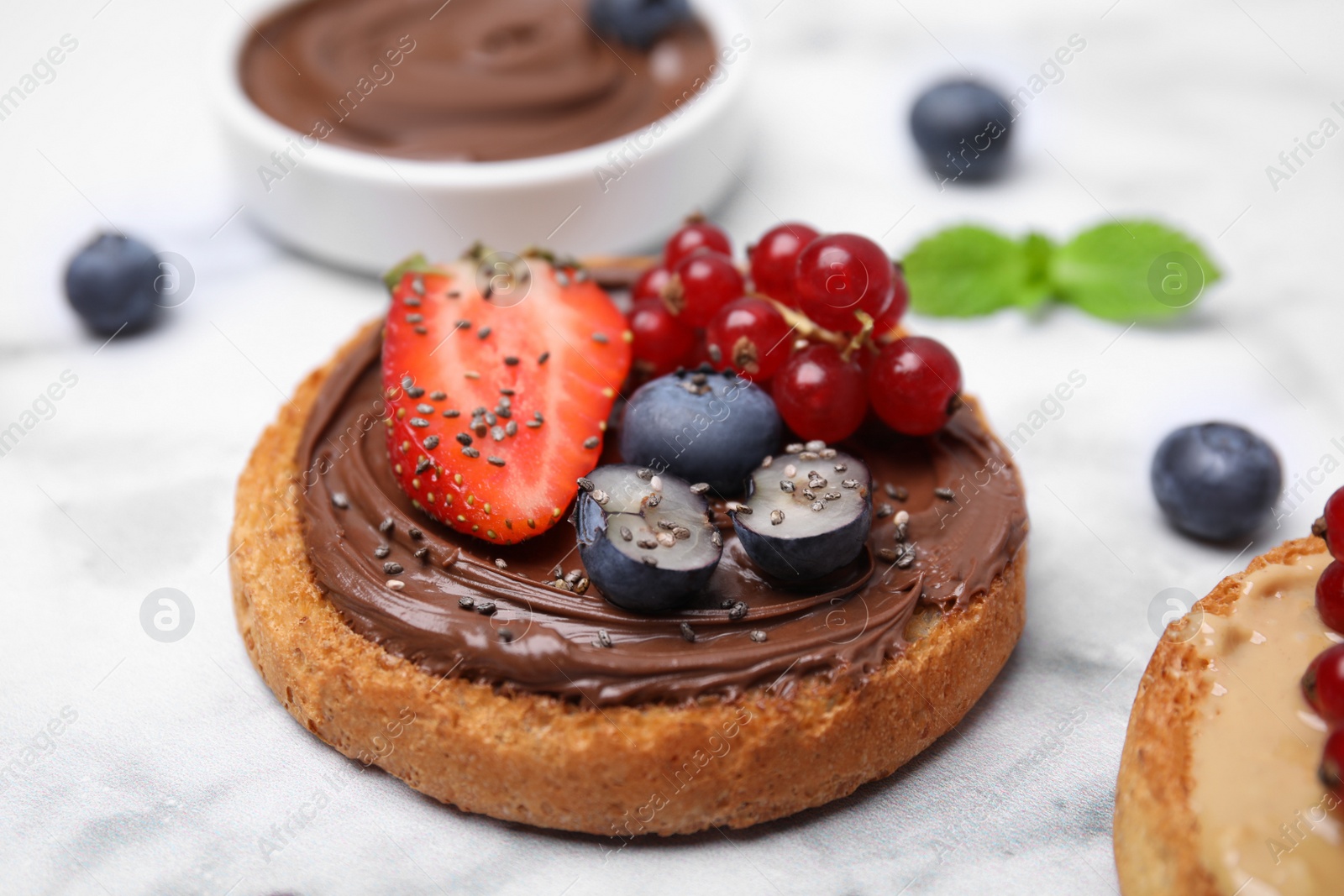 Photo of Tasty organic rusk with chocolate spread and sweet berries on white marble table, closeup