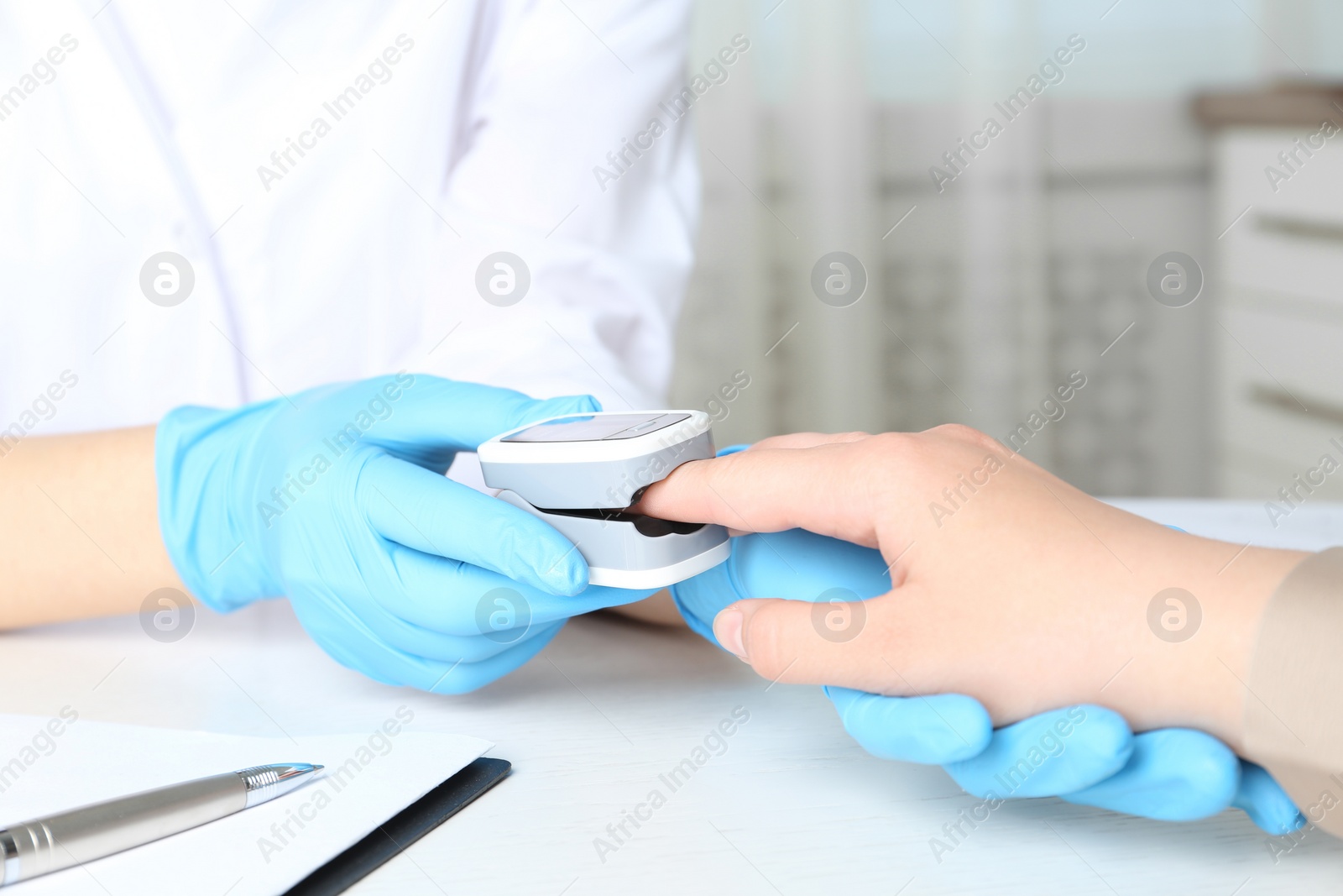 Photo of Doctor examining patient with fingertip pulse oximeter at white table in office, closeup