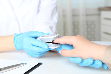 Photo of Doctor examining patient with fingertip pulse oximeter at white table in office, closeup