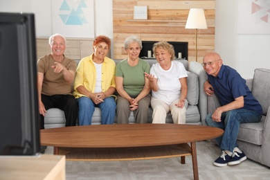 Happy elderly people watching TV together in living room