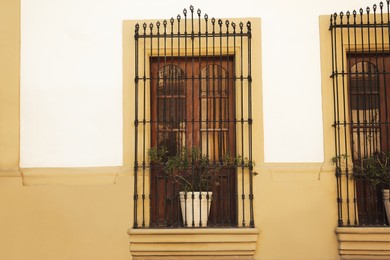 Photo of Beautiful windows with grills and potted plants on building, view from outdoors