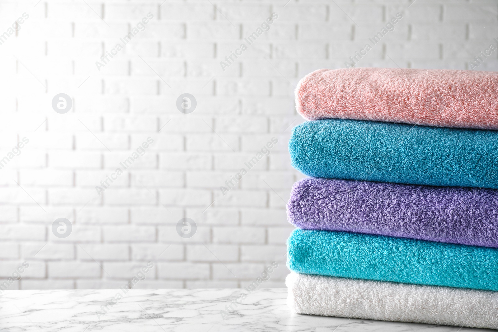 Photo of Stack of clean bath towels on white marble table. Space for text