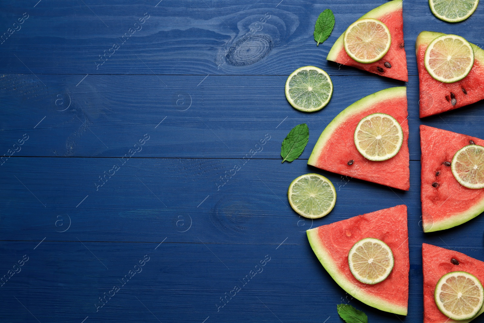 Photo of Tasty sliced watermelon and lime on blue wooden table, flat lay. Space for text